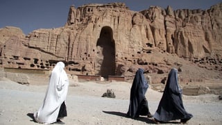 Frauen in Burkas laufen an dem Loch im Fels vorbei, wo einst die Buddhastatuen standen. Frauen in Burkas laufen an dem Loch im Fels vorbei, wo einst die Buddhastatuen standen.