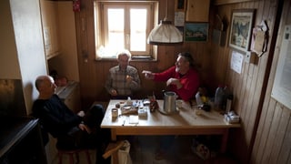 Drei Männer sitzen in einer kleinen Stube an einem Holztisch