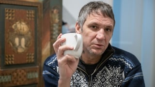 Ein Mann im Norweger-Pullover hält eine Kaffeetasse in der Hand und blick tin die Kamera.