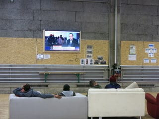 Asylbewerber sitzen ausf Sofa und schauen fern.