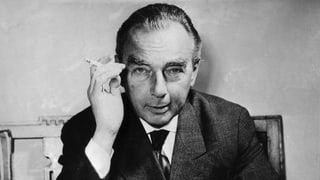 Poträtfoto von Erich Kästner, der direkt in die Kamera schaut. In seiner rechten Hand eine Zigarette. 