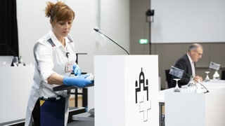 Eine Frau trägt Schutzhandschuhe und desinfiziert ein Rednerpult. Eine Frau trägt Schutzhandschuhe und desinfiziert ein Rednerpult.