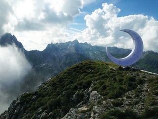 Grosse Installation einer Mondsichel vor einem Bergpanorama.