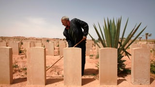 Ein Mann steht zwischen Reihen von Grabsteinen in einer wüstenartigen Landschaft.