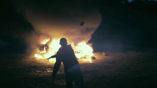 Szene: Ein junger Mann vor einem grossen Feuer.