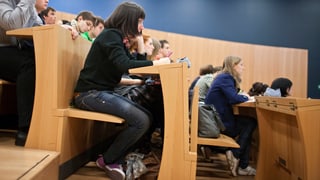 Drei abgestufte Reihen Sitzplätze in einem Hörsaal, Studierende hören zu.