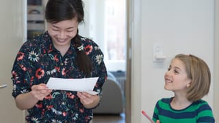 Ein frau schaut lachend auf einen Zettel, ein Mädchen steht lachend daneben und schaut ihr zu. Ein frau schaut lachend auf einen Zettel, ein Mädchen steht lachend daneben und schaut ihr zu.