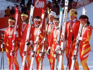 Gruppenfoto mit den erfolgreichen Skirennfahrerinnen und -fahrern. Sie tragen rot-gelbe Renndress und halten ihre Skier in der Hand.