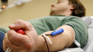 Ein Mann liegt auf einer Pritsche und spendet Blut. Er hat eine Nadel im Arm und einen Gummiball in der Hand.