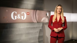 Frau mit blonden langen Haaren in einem roten Hosenanzug vor einer Betonwand mit der Aufschrift «G&G» Frau mit blonden langen Haaren in einem roten Hosenanzug vor einer Betonwand mit der Aufschrift «G&G»