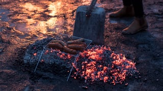 Ein Klappgrill mit Würsten über einem Gluthaufen