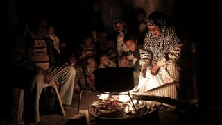 Eine elfköpfige Familie im Gazastreifen sitzt im Dunkeln um eine Feuerschale mit einer Pfanne darüber.