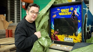 Ein Mann enthüllt einen alten, defekten Videospielautomaten im Freien