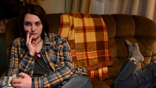 Eine Teenagerin sitzt mit ernstem Gesicht auf einer Couch