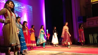 Acht tamilische Frauen in traditionellen, farbigen Gewändern auf einer Bühne. 