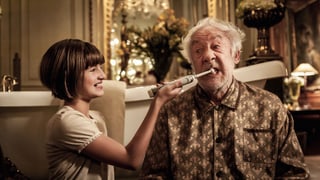 Ein Mädchen hilft einem ältern Mann beim Zähneputzen mit einer elektrischen Zahnbürste.