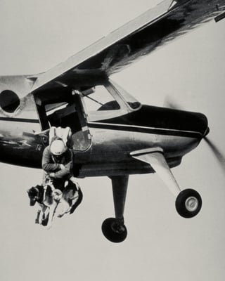 Rettungshelfer springt mit Hund aus Kleinflugzeug.