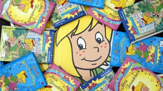 Kleines blondes Mädchen grinst inmitten von Büchern hervor Kleines blondes Mädchen grinst inmitten von Büchern hervor