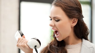 Eine Frau schreit verärgert in einen Telefonhörer.