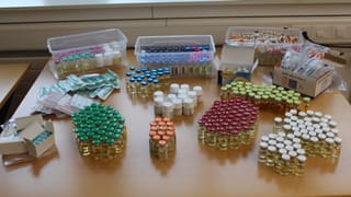 Fläschchen, Döschen, Spritzen und Tabletten in verschiedenen Farben stehen auf einem Tisch.