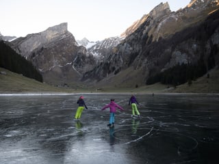 Drei Mädchen laufen auf dem spiegelglatt zugefrohrenen See Schlittschuh. 