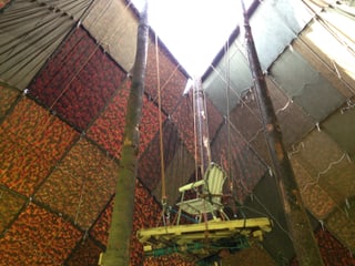 Zu sehen ist ein viele Meter hohes Zelt in der Innenansicht. An zwei Baumstämmen führt ein selbst gebauter Lift nach oben.