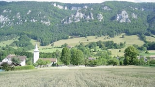Blick über ein Feld auf die Kirche von Grandval