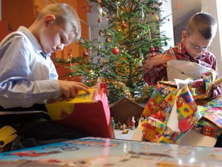 Zwei Kinder begutachten ihre Weihnachtsgeschenke unter dem Christbaum.