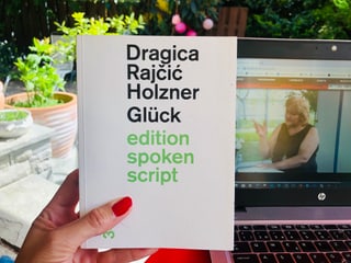 Das Buch «Glück» von Dragica Rajčić Holzner wird vor den Laptop gehalten