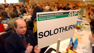 Viele Leute an einer Parteiversammlung, auf eine Tisch steht ein Schild, darauf steht SVP Solothurn