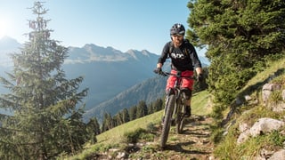 Ein Biker fährt auf einem schmalen Pfad, im Hintergrund sind die Churfirsten abgebildet. Ein Biker fährt auf einem schmalen Pfad, im Hintergrund sind die Churfirsten abgebildet.