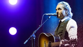 Stephan Eicher mit Gitarre vor einem Mikrofon.