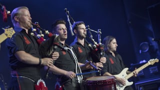 Die Red Hot Chilli Pipers spielen auf einer Bühne Dudelsack, E-Gitarre und die Trommel.