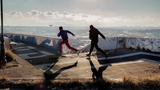 Zwei Jungen rennen im Zwielicht über eine Terrasse.