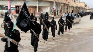 Schwarz gekleidete, vermummte und bewaffnete Dschihadisten defilieren auf einer Strasse.