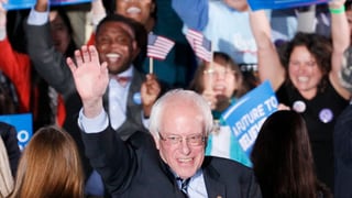 Sanders hebt, umringt von Anhängern mit Schildern und Fähnchen, seine rechts Hand.