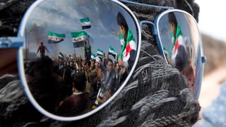 In den Gläsern einer Sonnenbrille spiegeln sich demonstrierenden Syrern in Jordanien. 