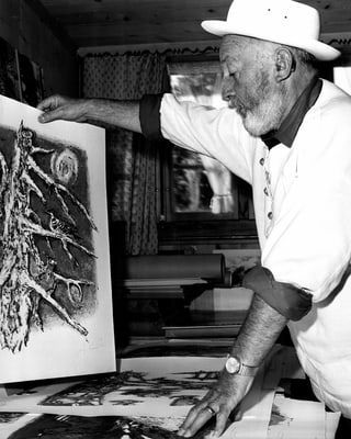 Der Künstler Alois Carigiet mit einem Bild in der Hand in seinem Arbeitsraum.