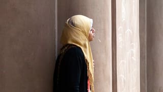 Eine Frau mit Hidschab steht vor einer Moschee.
