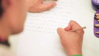 Erwachsene Person schreibt an einem Kurs für Illettristen Sätze auf einen Zettel.