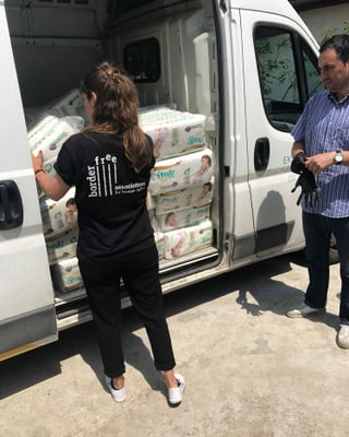 Eine schwarz gekleidete Frau lädt Windeln aus einem weissen Bus aus. Eine schwarz gekleidete Frau lädt Windeln aus einem weissen Bus aus.