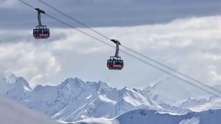 Zwei Bergbahn-Gondeln kreuzen sich vor einer Bergkulisse. 