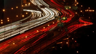 Nachtaufnahme einer Strassse mit Autos, die eine Lichtspur nach sich ziehen.