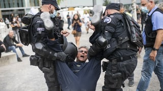 Zu sehen Polizisten, die einen Demonstranten wegtragen.