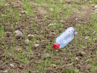 Eine leere Petflasche auf einem Acker.
