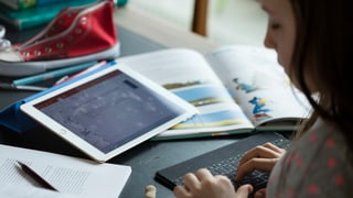 Ein Schülerin macht ihre Hausaufgaben mit Tablet und Schulbuch. 