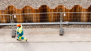 Ein Baustellenarbeiter geht einer Abschrankung aus Eisengittern entlag, Perspektive von oben.