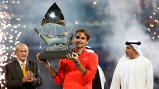 Roger Federer präsentiert auf dem Court in Dubai die Siegestrophäe.