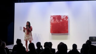 Eine Frau auf einer Bühne in einem blutverschmierten Kleid steht neben einem blutroten Bild.