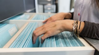 Eine Frau sucht in einem Hängeregister nach einem Patientendossier Eine Frau sucht in einem Hängeregister nach einem Patientendossier